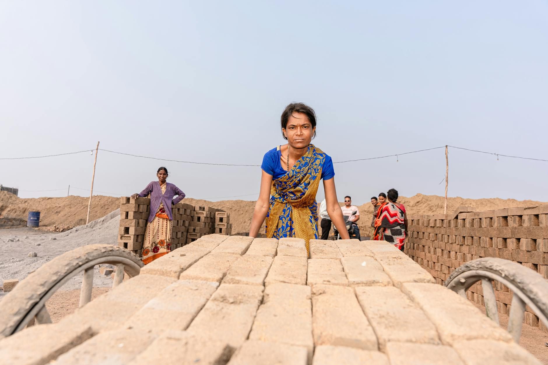 A group of workers in traditional attire, transporting bricks at a rural worksite. Captured in India.