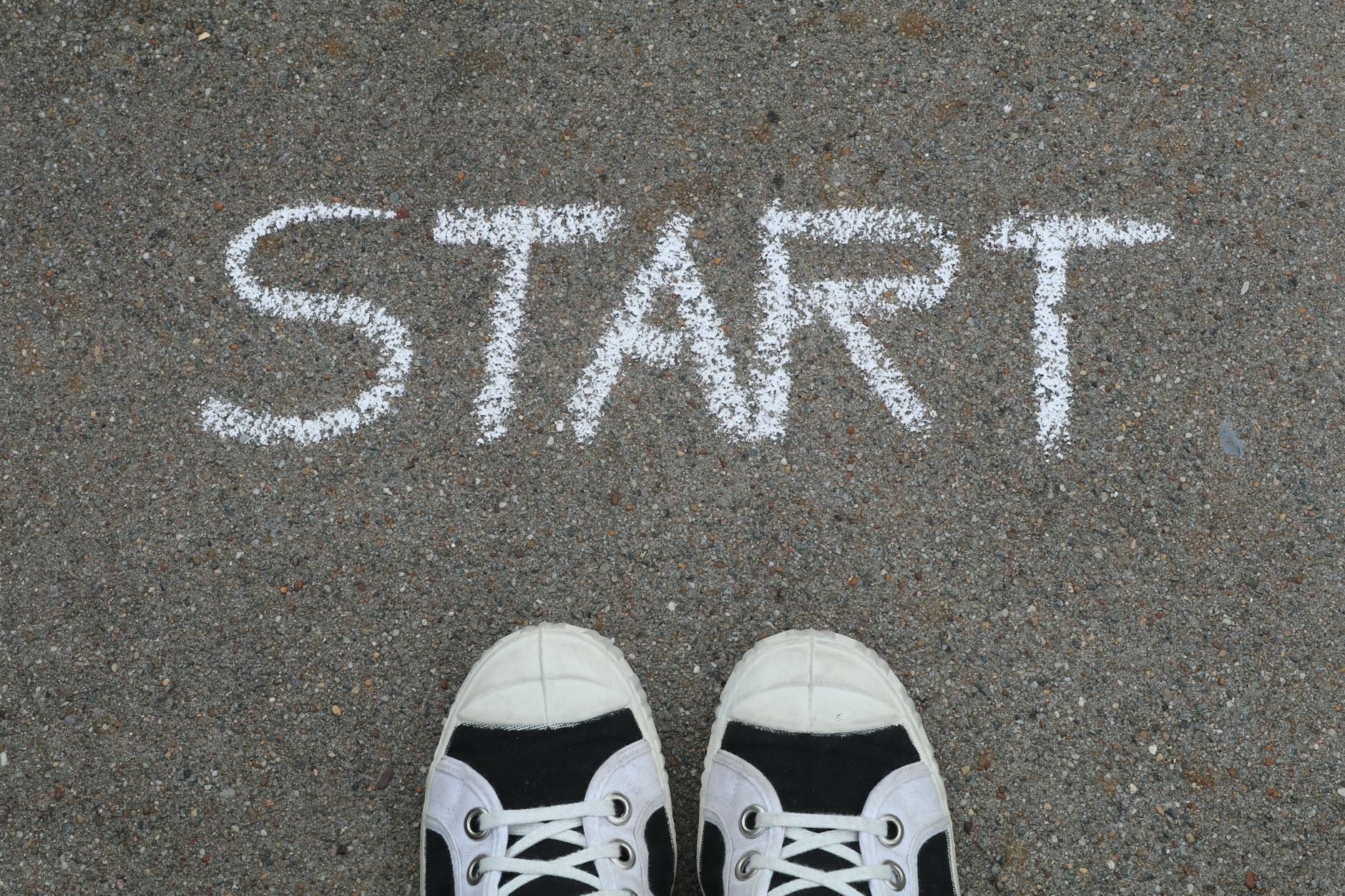 Close-up of sneakers and a 'START' chalk drawing on pavement, symbolizing new beginnings.