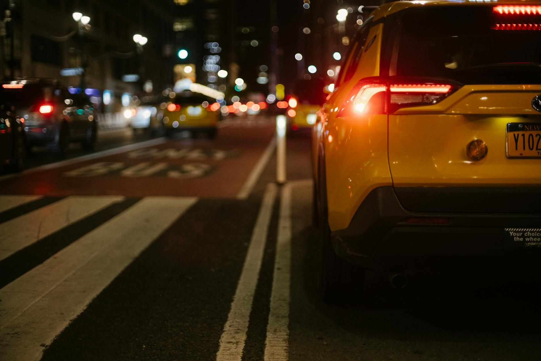A yellow taxi navigates the busy city street at night, capturing urban nightlife.